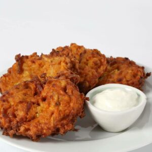 Four Sweet Potato Pancakes are served on a white plate with a small bowl of creamy dipping sauce.