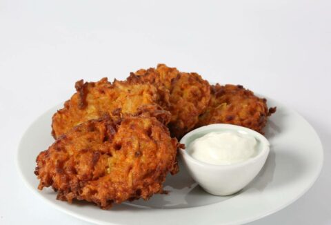 Four Sweet Potato Pancakes are served on a white plate with a small bowl of creamy dipping sauce.