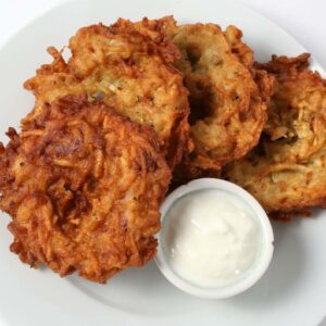 12 - Potato Pancakes: Four crispy potato pancakes are served on a white plate with a small cup of white dipping sauce.