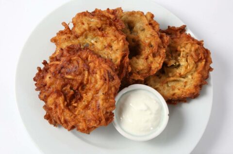 12 - Potato Pancakes: Four crispy potato pancakes are served on a white plate with a small cup of white dipping sauce.