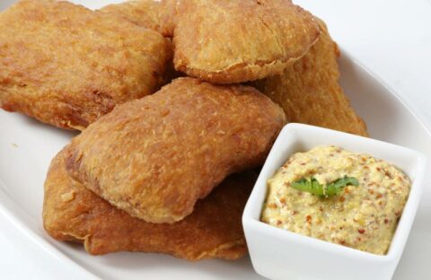 Four Sweet Potato Snackers are served on a white plate beside a small dish of grainy mustard dipping sauce, garnished with a sprig of herb.
