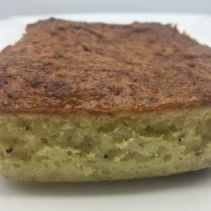 A close-up of a rectangular slice of 5 LBS - Potato Pudding, featuring a golden-brown crust on top and a light, airy interior.
